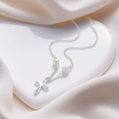 Silver necklace with a cross pendant and pearls on a soft fabric background